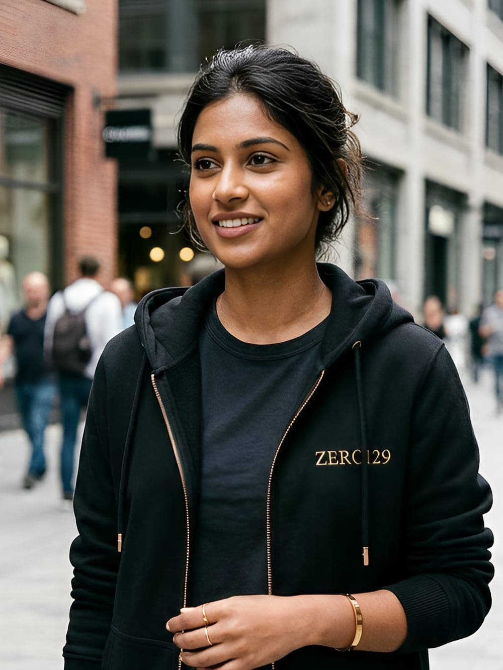 Model in the black Zero129 zip hoodie with gold embroidery and a rose-gold zip, on a city street